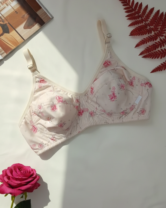 Floral-patterned bra on a white surface with a pink rose and red leaves.