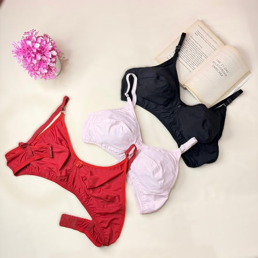Red, white, and black bras on a light surface with a pink flower and book.